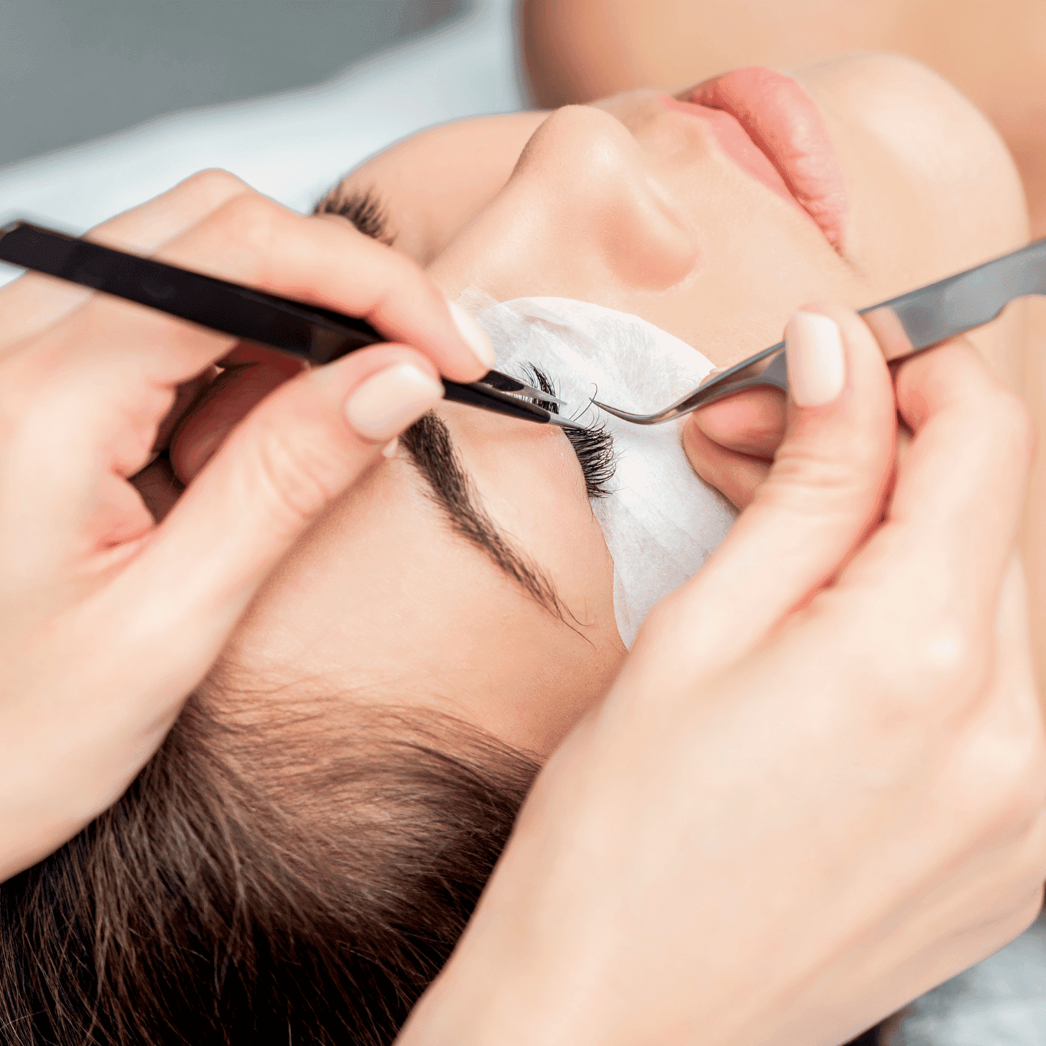 Eyelash extension procedure with tweezers and protective eye pads.