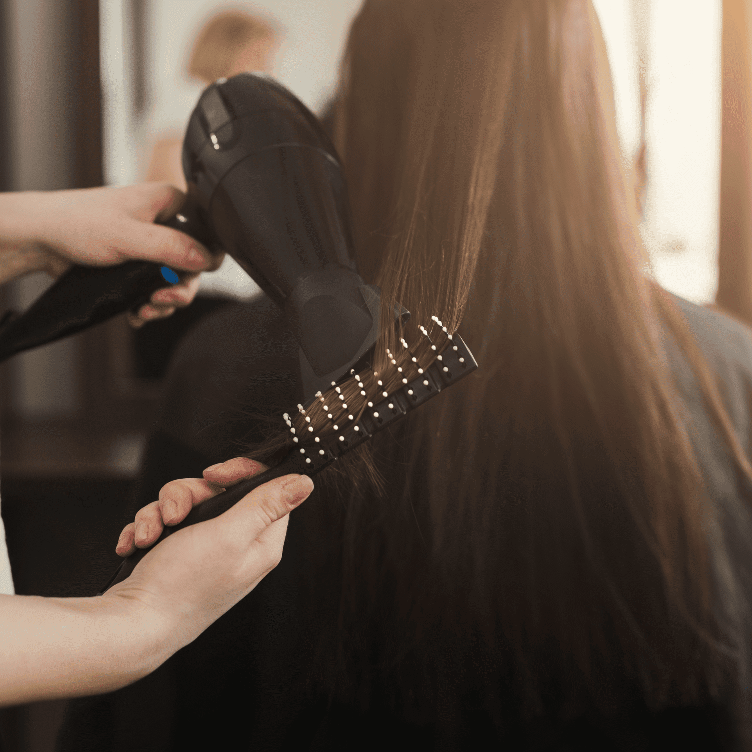 A stylist blow-dries long, brown hair in a salon setting.